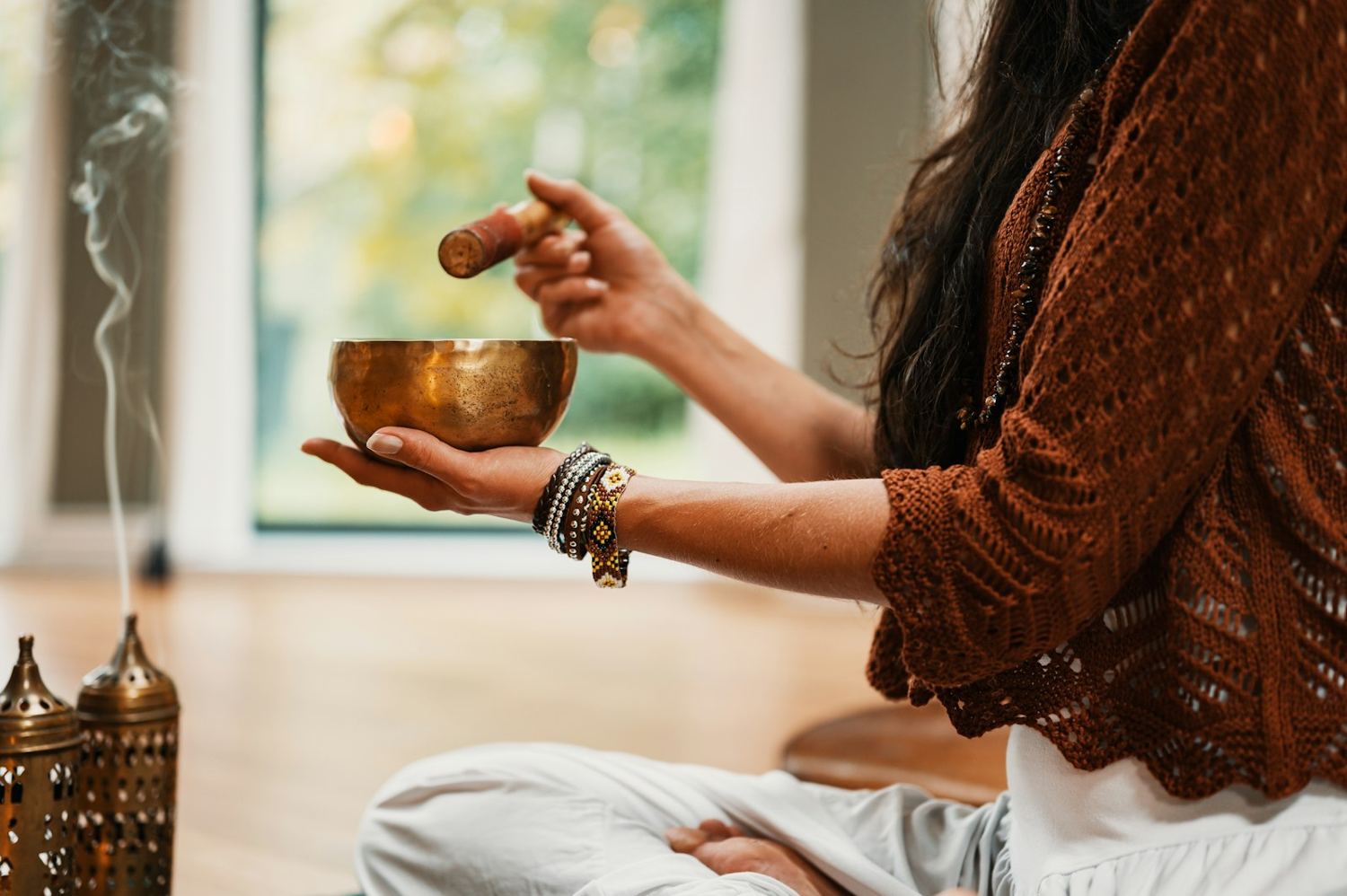 Hands holding a brass singing bowl beside a curl of incense smoke